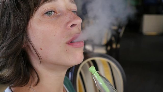 Young woman portrait smoking hookah in a bar breath out smoke slow motion