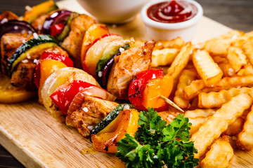 Kebabs - grilled meat with french fries and vegetables on wooden background 