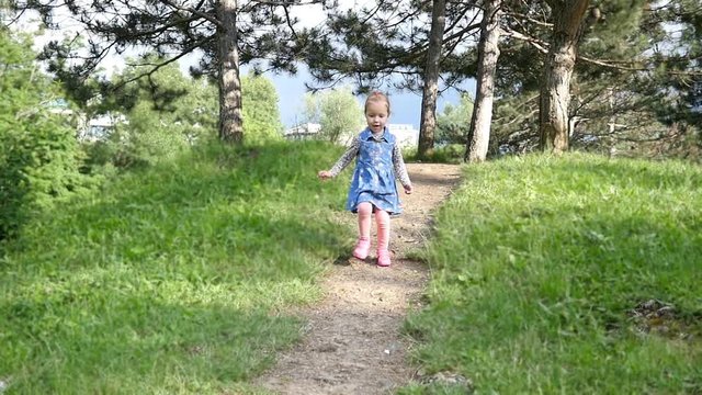 Little girl happily running down the hill in a green park slow motion