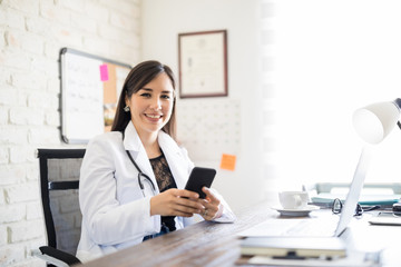 Happy female doctor with phone at office