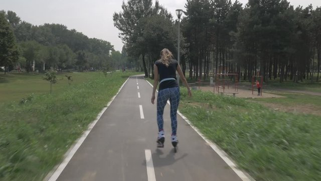 White handsom brown hair girl in tight blue pants woman riding roller skates on bike road in park, during summer day