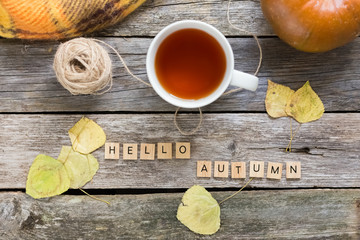 Autumn fall flat lay, top view. Fall leaves, mug of tea. pumpkin with inscription hello autumn on rustic wooden background. Fall autumn concept.