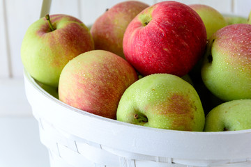 White basket with red and green apples on front of white wooden wall. Harvest concept
