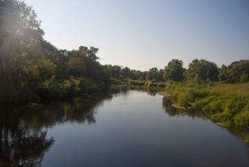 Landscape of the middle zone of Russia: the Nara River with low banks, overgrown with green grass and trees