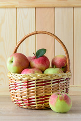 Wooden basket with red and green apples on front of brown wooden wall. Harvest concept