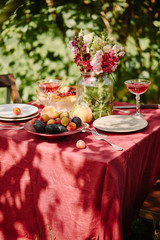 yummy fruits, wineglasses and bouquet of flowers on table in garden