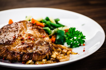 Grilled steak with vegetables on wooden background