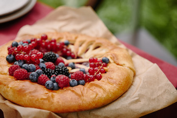 tasty pie with raspberries, currants and blueberries on table in garden
