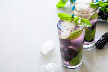 Refreshing lemonade with blackberry, ice and mint on gray wooden background. Summer drink concept