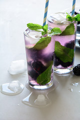 Refreshing lemonade with blackberry, ice and mint on gray wooden background. Summer drink concept