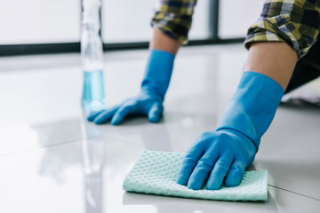 Husband housekeeping and cleaning concept, Happy young man in blue rubber gloves wiping dust using a spray and a duster while cleaning on floor at home