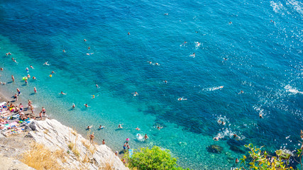 The top view and the beach. View from the high rocky shore. Azure-blue clear water. People swim in the beach. Black sea, Crimea