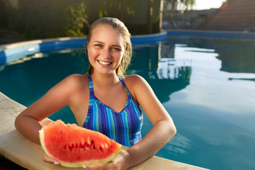 Pretty tanned slim young woman holds slice red watermelon over blue pool, relaxing on tropical island in resort, eating healthy food. Fruit summer diet. Vegetarianism and vegan lifestyle.