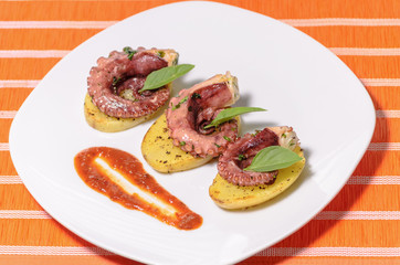 Platillo gourmet de pulpo con especias en una cama de patatas y salsa picante, en un plato blanco con mantel, platillo mexicano del mar