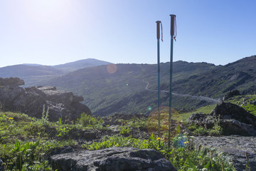 pair of trekking poles on the background of a mountain path traversing in the distance in the sunlight