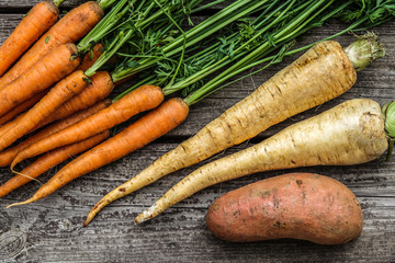 Close up of a bundle of carrots, parsnip and sweet potato on a rustic wooden table. Concept for root vegetable, organic raw food, farming and harvest.