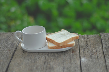 White bread and glass placed on the table in the morning.On the breakfast table there was a glass of coffee and a plate of bread.Breakfast set on wooden floor in the morning.