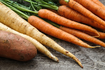 Close up of a bundle of carrots, parsnip and sweet potato on a rustic wooden table. Concept for root vegetable, organic raw food, farming and harvest.