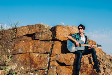 Fototapeta premium the guy plays guitar sitting big on the rocks