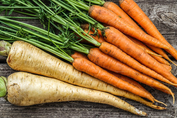 Close up of a bundle of carrots and parsnip on a rustic wooden table. Concept for root vegetable, organic raw food, farming and harvest. - obrazy, fototapety, plakaty