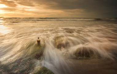 Sunset at the beach with natural coastal rocks on the ground. soft focus due to slow shutter.