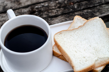 White bread and glass placed on the table in the morning.On the breakfast table there was a glass of coffee and a plate of bread.Breakfast set on wooden floor in the morning.