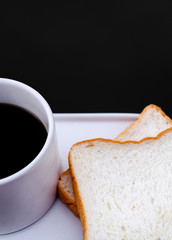 White bread and glass placed on the table in the morning.On the breakfast table there was a glass of coffee and a plate of bread.Breakfast set on wooden floor in the morning.