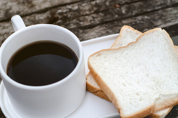 White bread and glass placed on the table in the morning.On the breakfast table there was a glass of coffee and a plate of bread.Breakfast set on wooden floor in the morning.
