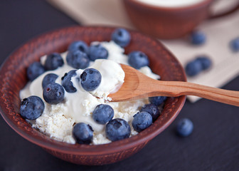 Cottage cheese with sour cream and blueberries in a clay cup.