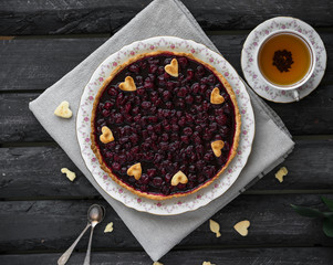 homemade tart with cherry filling on linen cloth on dark brown wooden backdrop, cup of tea, dessert