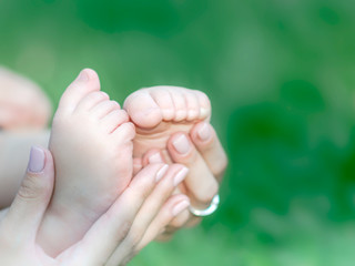 Mother holding feet of newborn baby on green grass background. The concept of maternal tenderness, care, love and health. Copy space.