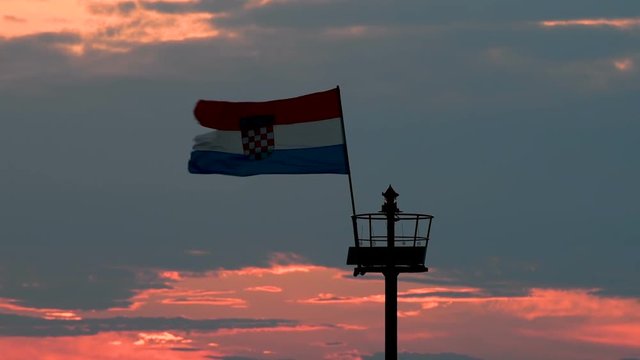 Stone pier with lighthouse and flying Croatian flag in sunset, zoom in close up