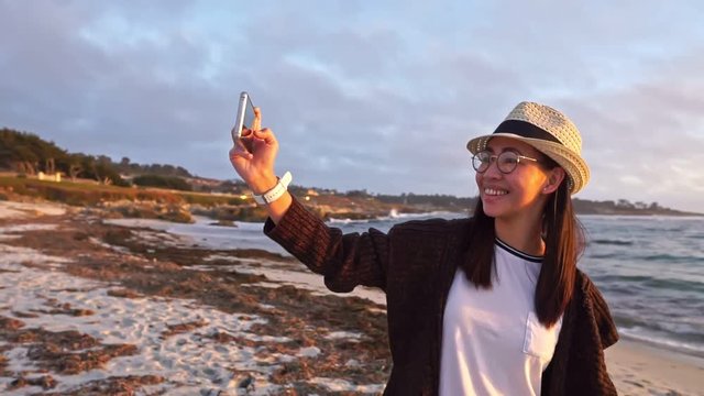 Young lady taking a selfie with the sunset on a beach