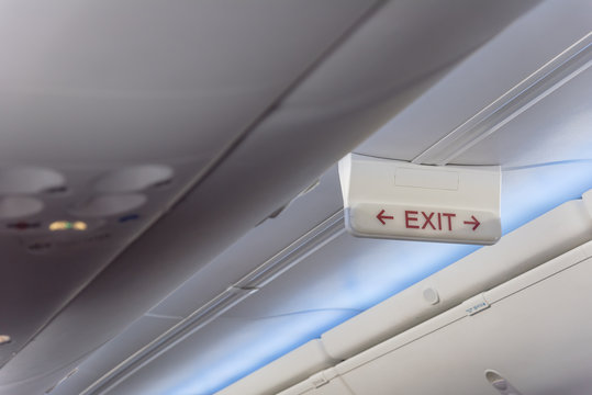 Emergency exit sign with red arrow on ceiling of airplane. Illuminated evacuation symbol underneath the overhead compartments. Shining signboard show escape of emergency, urgency, firer concept