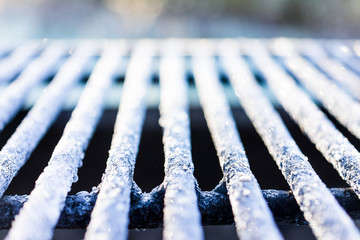 White frost ice crystals on metal grill outside in morning sunlight macro closeup with shiny bokeh