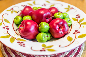 Closeup of colorful decorative plate with fake red, green apples pile on kitchen dining table in home