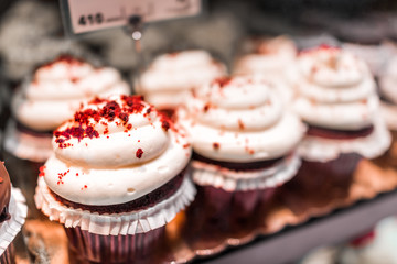 Macro closeup of red velvet cupcakes on display in bakery in muffin paper liners with white cream cheese icing