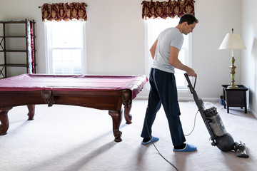 Young man house husband vacuuming using vacuum hoovering carpet floor inside interior of house...