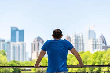 Young man standing leaning on railing in Piedmont Park in Atlanta, Georgia with scenic cityscape skyline of urban city skyscrapers downtown, Lake Clara Meer - obrazy, fototapety, plakaty