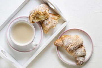 cornetti con  cappuccino o caffe latte  e colazione in vassoio bianco e tazza e piatti bianchi bordati di rosa
