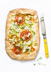 Feta, zucchini, tomatoes, thyme savory pie on a light background, top view. Delicious snack, appetizer in a mediterranean style