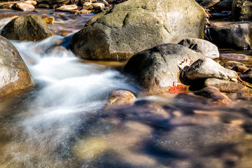 Closeup of shallow rock stream with smooth running water and waterfall in autumn, stones and long...
