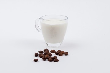 A glass mug full of milk next to coffee beans on a white stench. Isolated