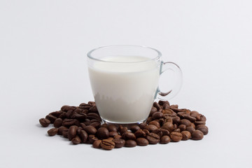 A glass mug full of milk is standing in a pile of coffee beans