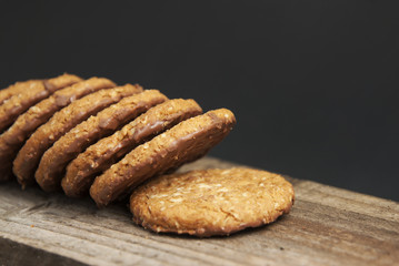 Oatmeal cookies or biscuits with oats, nuts, eggs and flour on brown dark woodenboard with black background, side view.