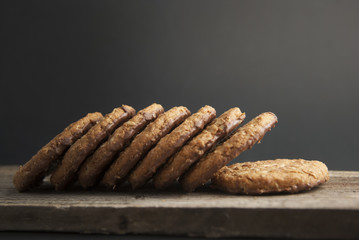 Oatmeal cookies or biscuits with oats, nuts, eggs and flour on brown dark woodenboard with black background, side view.
