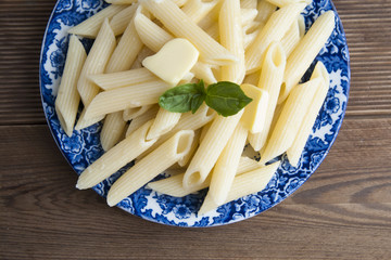 Cooked penne pasta with butter and cheese and basil in vintage beautiful blue plate on wooden table. Isolated.