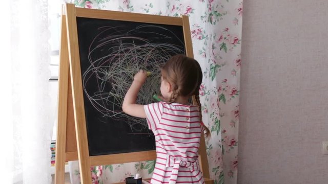 Little Preschool Girl Writing on Blackboard. Toddler girl holding chalk and drawing.