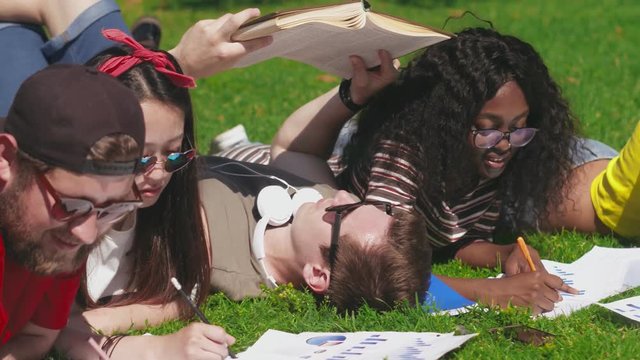 Young adults lying and studying on campus lawn