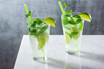 Two Cold Mojito Cocktails Made with Rum, Fresh Mint, and Limes In Glasses on Marble Bar Counter